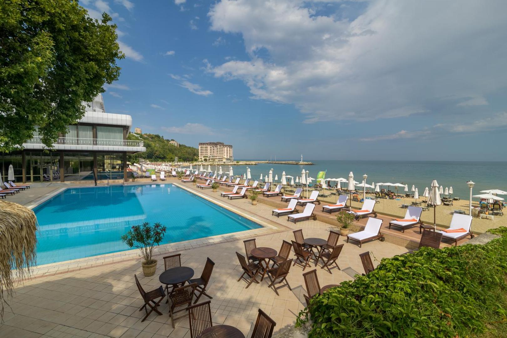 The Palace Hotel teritorija ar āra baseinu, pludmales zonu un terasi — skats uz kūrorta ēkām un jūras krastu