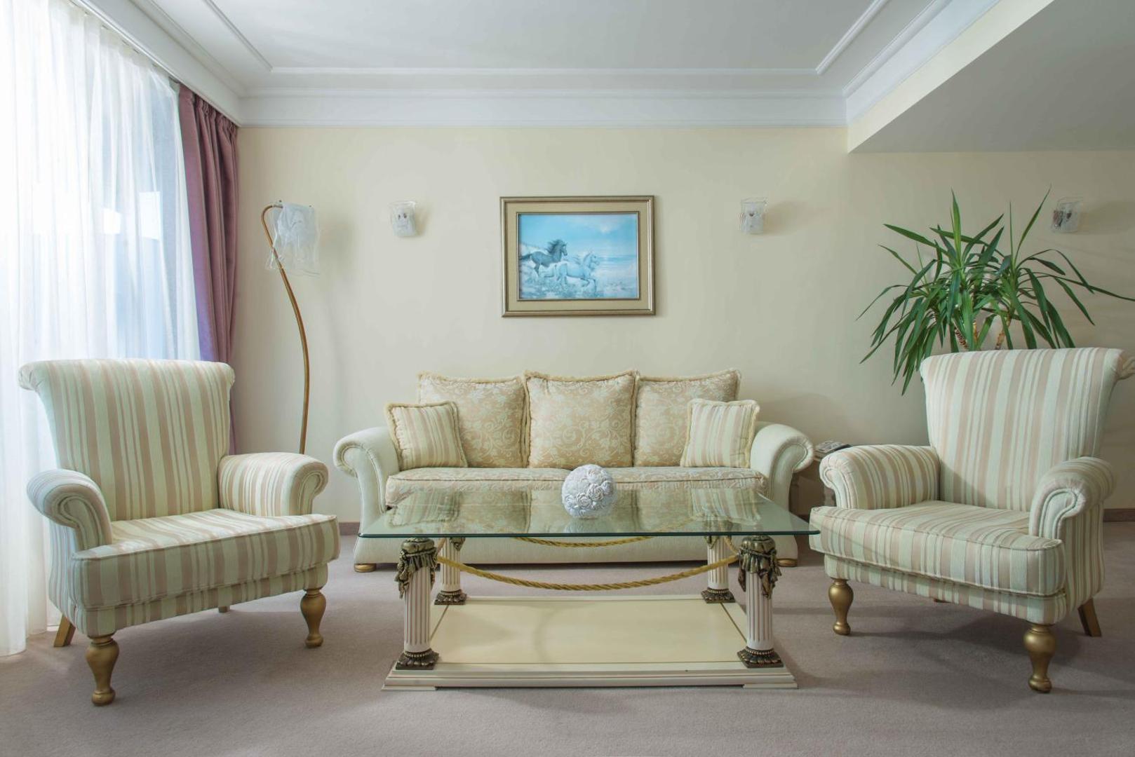 The Palace Hotel viesistabas zona ar klasisku dīvānu, atpūtas krēsliem un stikla galdiņu — elegants interjers gaišos toņos