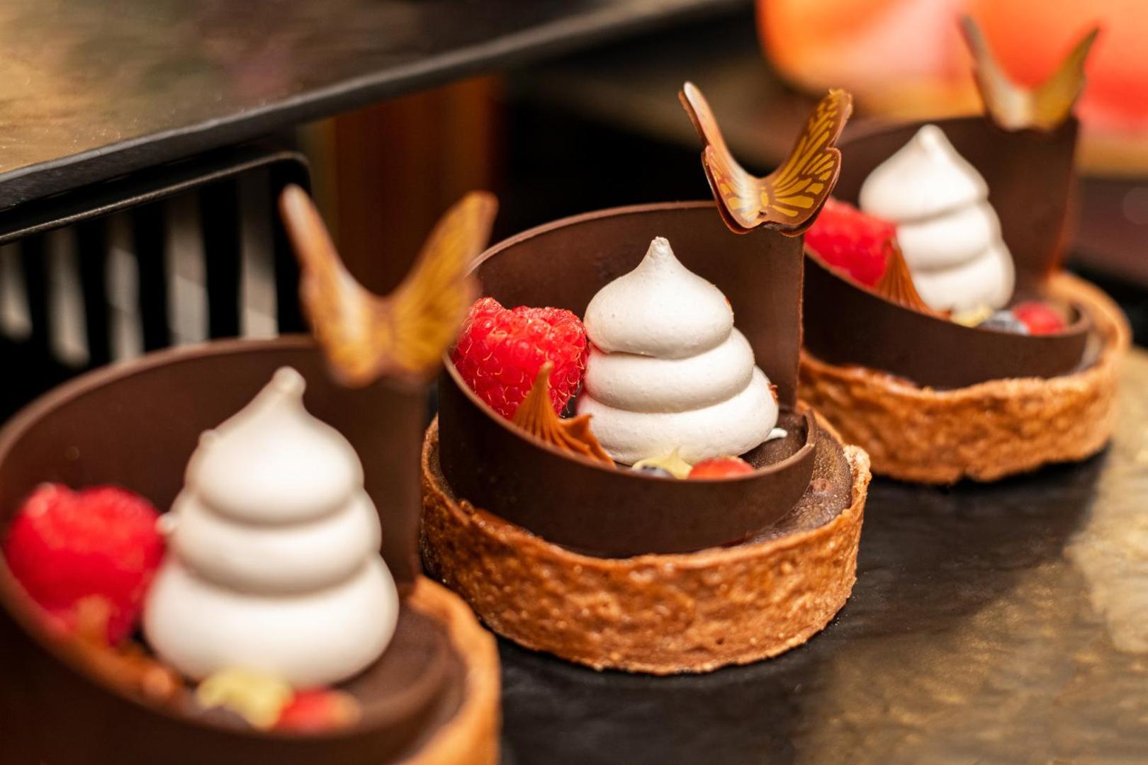 The Palace Hotel restorāna deserti — šokolādes groziņi ar bezē krēmu un svaigām avenēm, dekorēti ar tauriņu motīviem