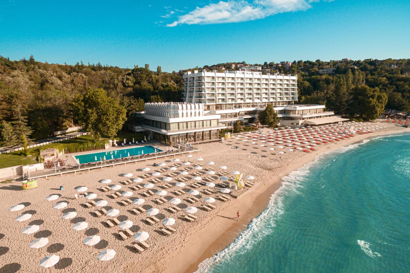 The Palace Hotel skats no putna lidojuma uz plašo smilšu pludmali, āra baseinu un viesnīcas ēku Saulainajā krastā, Bulgārijā