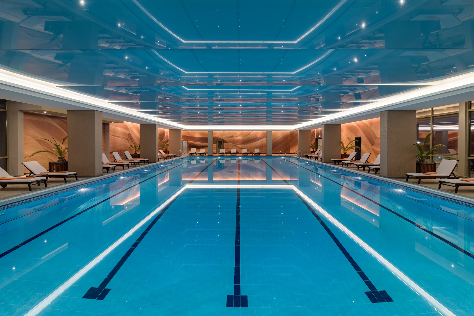 The Palace Hotel iekštelpu baseins ar zilu apgaismojumu un atpūtas krēsliem — plaša spa zona relaksācijai jebkuros laikapstākļos