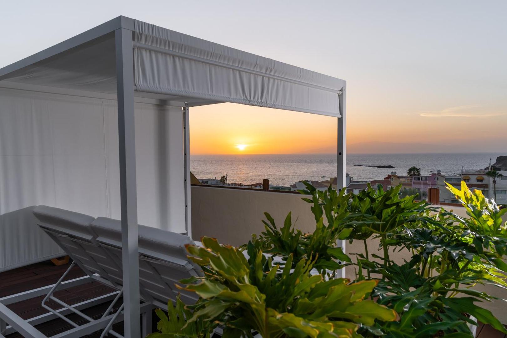 Saulrieta skats no Hovima Jardin Caleta terases ar atpūtas gultu un tropiskiem augiem Tenerifes piekrastē