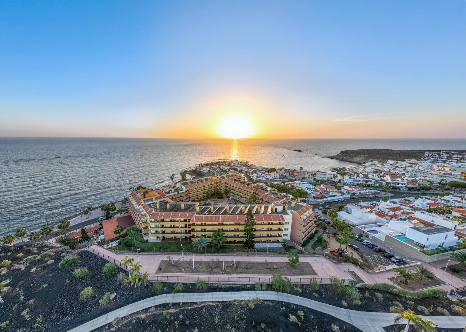 Hovima Jardin Caleta viesnīcas panorāmas skats Tenerifē saulrieta laikā — ēku komplekss pie okeāna krasta līnijas La Kaletas ciemata piekrastē