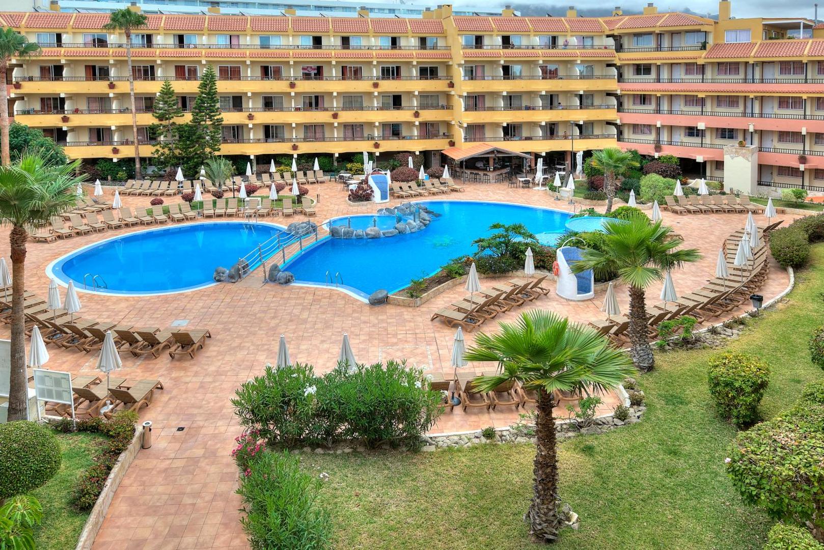 Skats no augšas uz Hovima Jardin Caleta viesnīcas baseiniem, dārzu un terasēm Tenerifes piekrastē saulainā dienā.