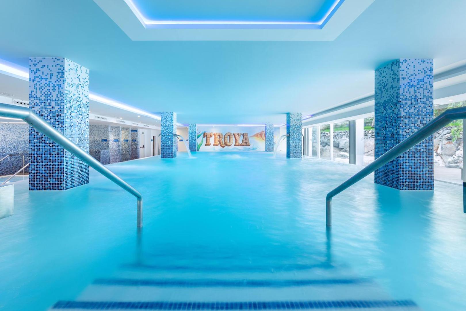 Alexandre Hotel Troya iekštelpu baseins ar zilu mozaīkas apdari un ūdens kaskādēm Tenerifē — plaša spa zona relaksācijai