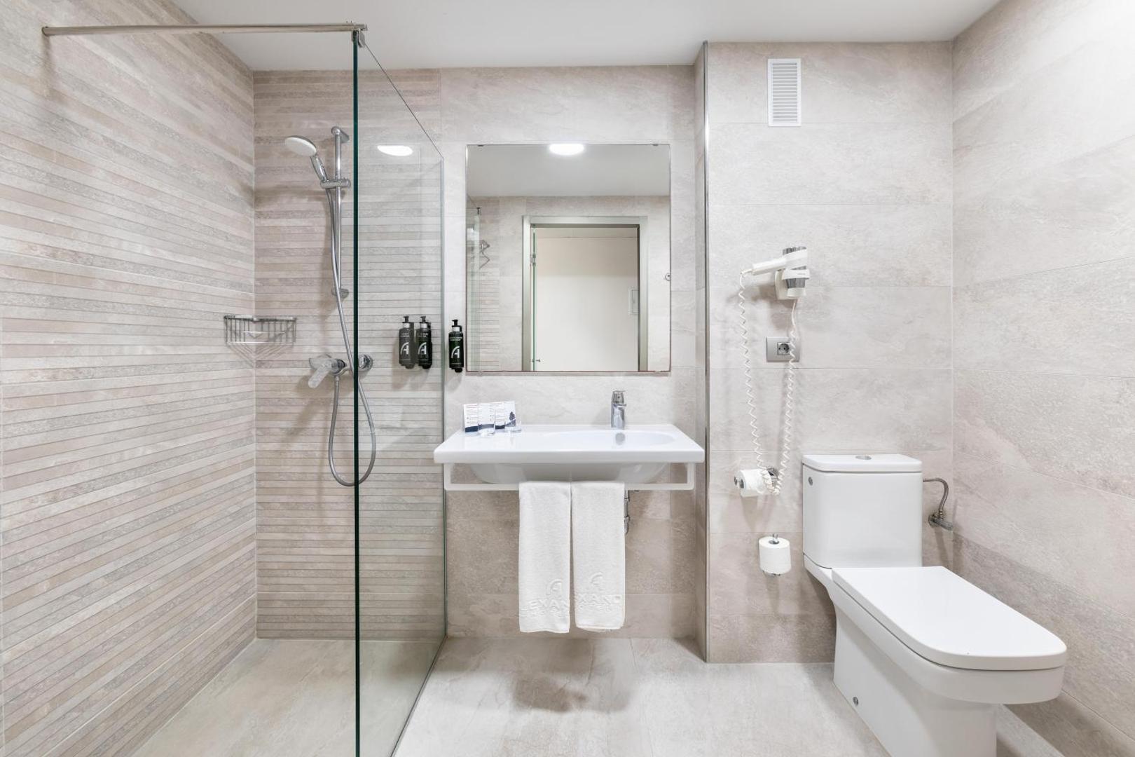 Alexandre Hotel Troya gaiša un mūsdienīga vannas istaba ar stiklotu dušas kabīni, spoguli un gaišām flīzēm Tenerifes kūrortā