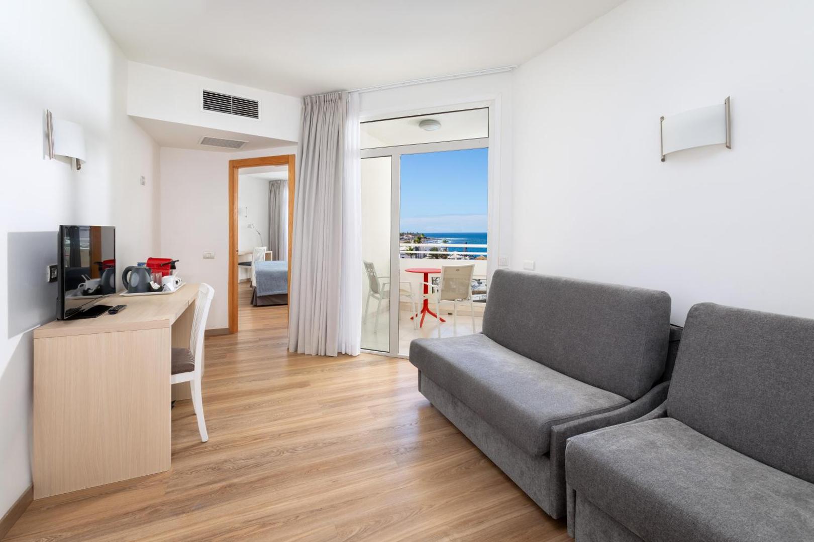 Alexandre Hotel Troya ģimenes numura viesistabas zona ar dīvānu, rakstāmgaldu un izeju uz balkonu ar skatu uz okeānu