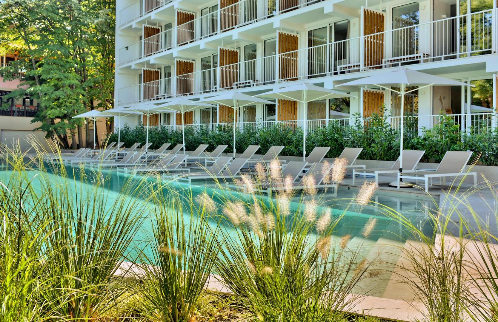 Ibis Styles Golden Sands Roomer Hotel baseina zona ar sauļošanās krēsliem un saulessargiem pie viesnīcas fasādes