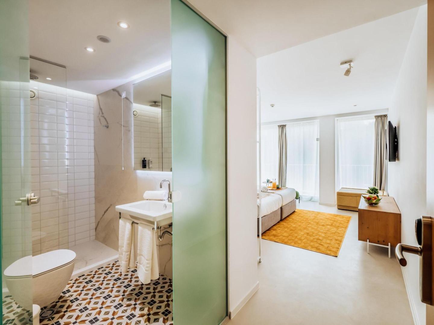 Ibis Styles Golden Sands Roomer numura vannasistaba ar dušu un skatu uz guļamzonu — mūsdienīgs dizains un rakstainas flīzes