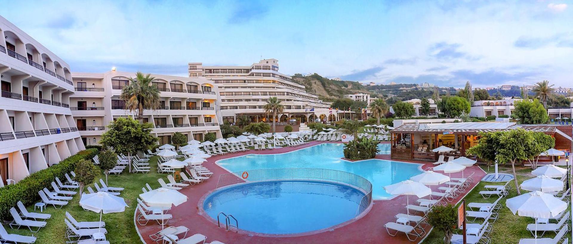 Sol by Melia Cosmopolitan Rhodes viesnīcas teritorija ar lielu āra baseinu, saulessargiem un daudzstāvu numuru korpusiem Rodas salā, Grieķijā