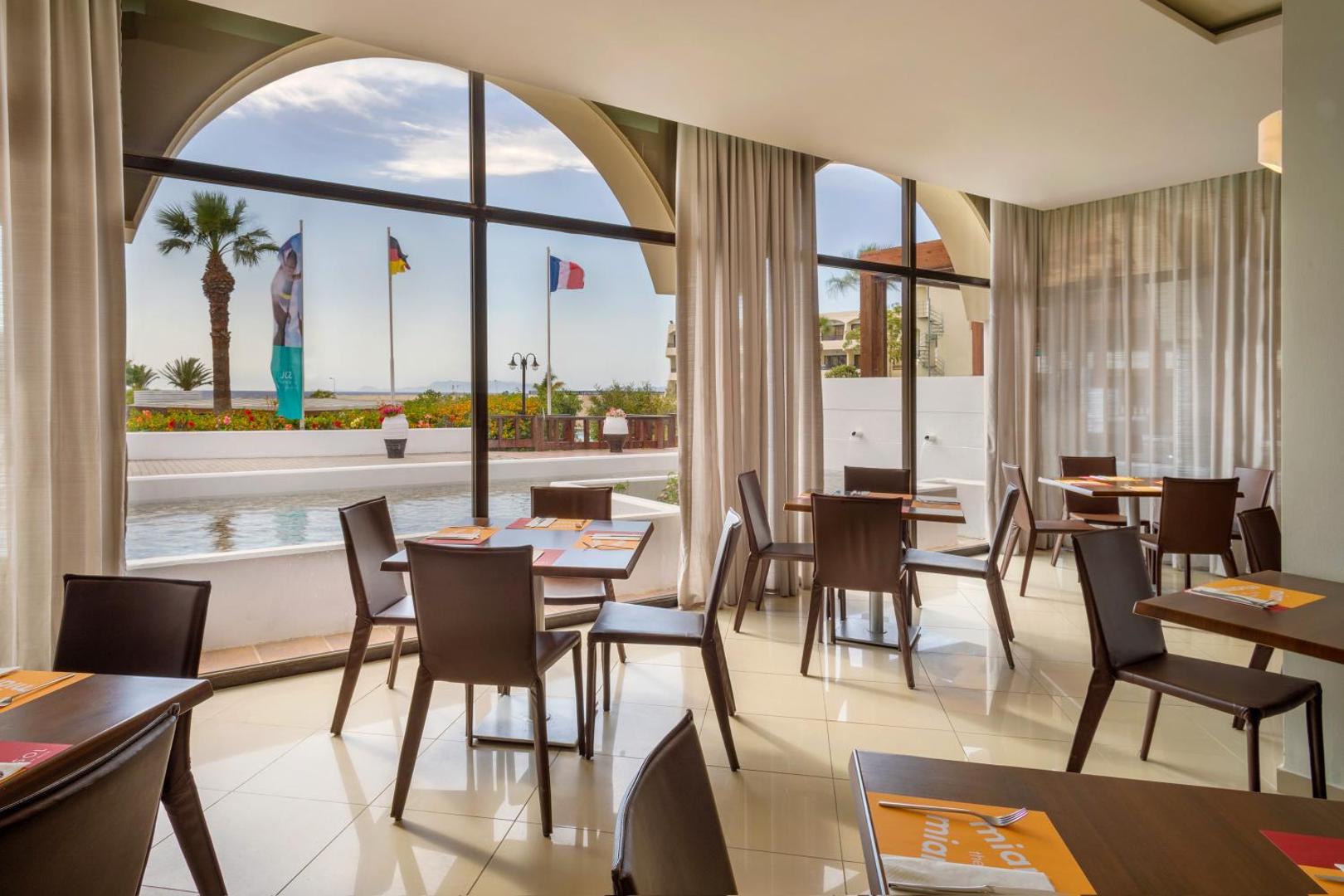 Sol by Melia Cosmopolitan Rhodes viesnīcas restorāns ar skatu uz baseinu un palmām Rodas salā, Grieķijā — gaišs interjers ar lieliem logiem.