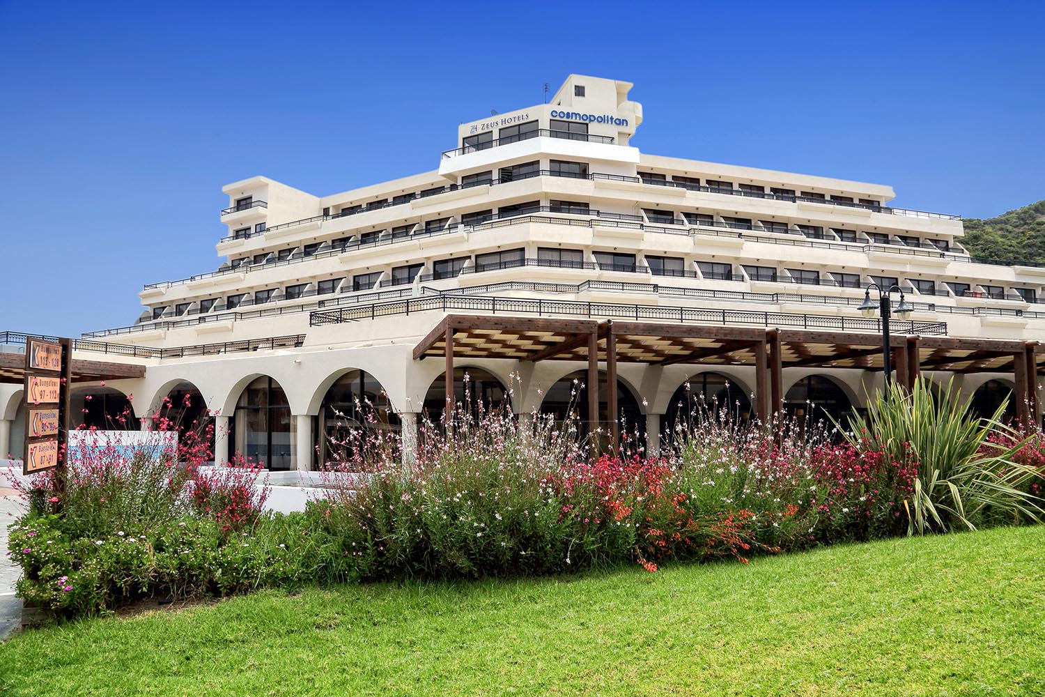 Viesnīcas Sol by Melia Cosmopolitan Rhodes galvenā ēka Rodas salā ar terasēm, koptu zālienu un ziedošām puķu dobēm saulainā dienā