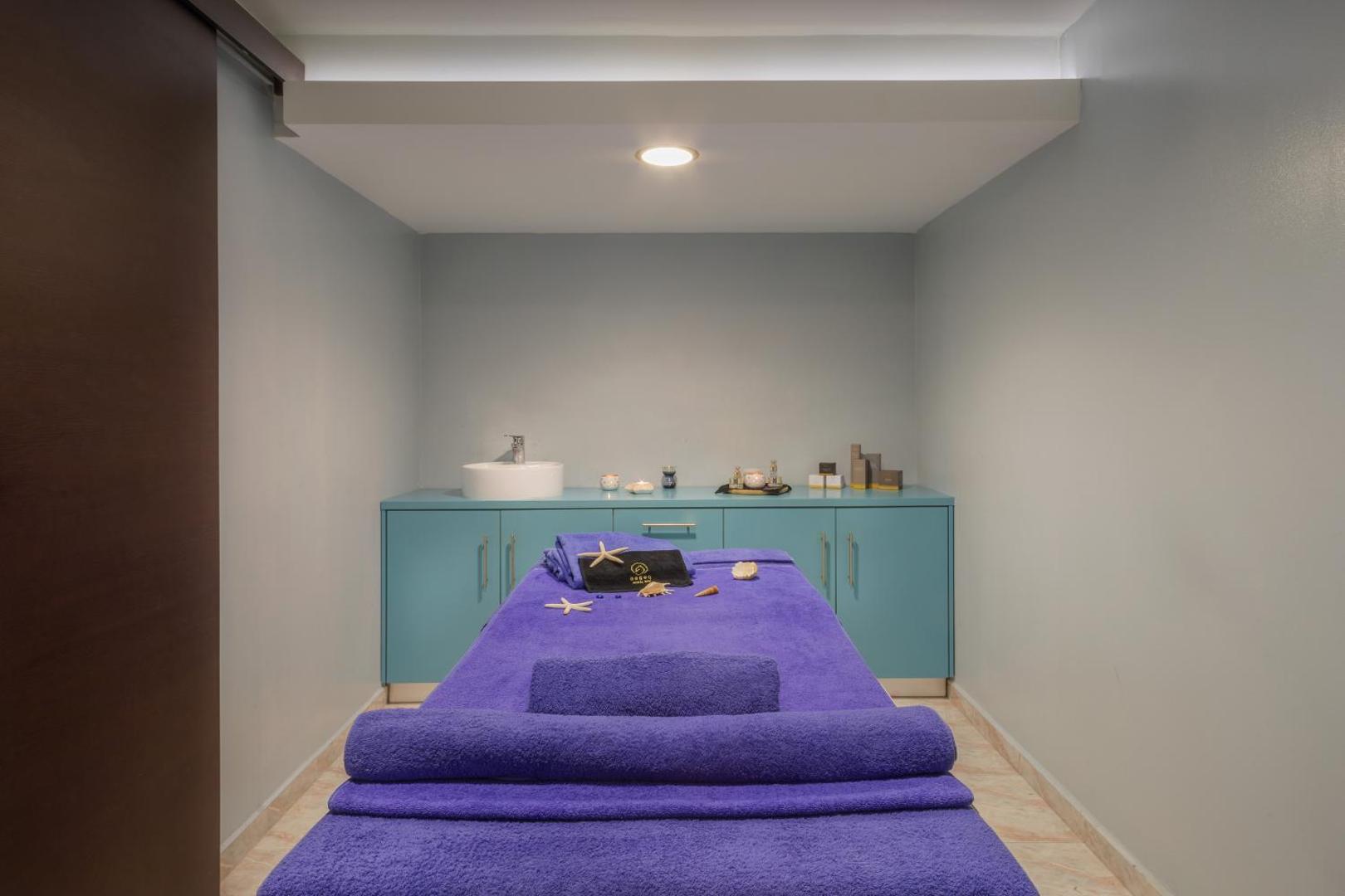 Sol by Melia Cosmopolitan Rhodes spa procedūru telpa ar masāžas galdu, violetiem dvieļiem un dekoratīvām jūras zvaigznēm Rodas salā.