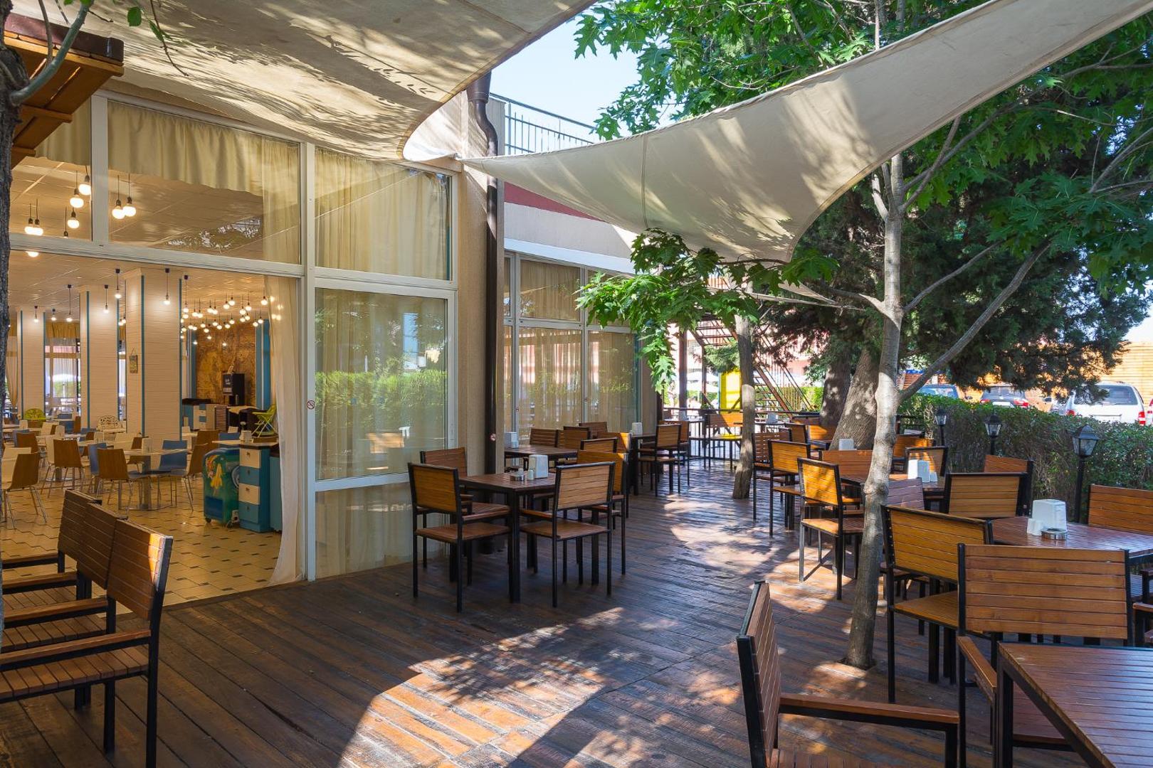 MPM Hotel Astoria āra restorāna zona uz koka klāja zem nojumēm un koku ēnā