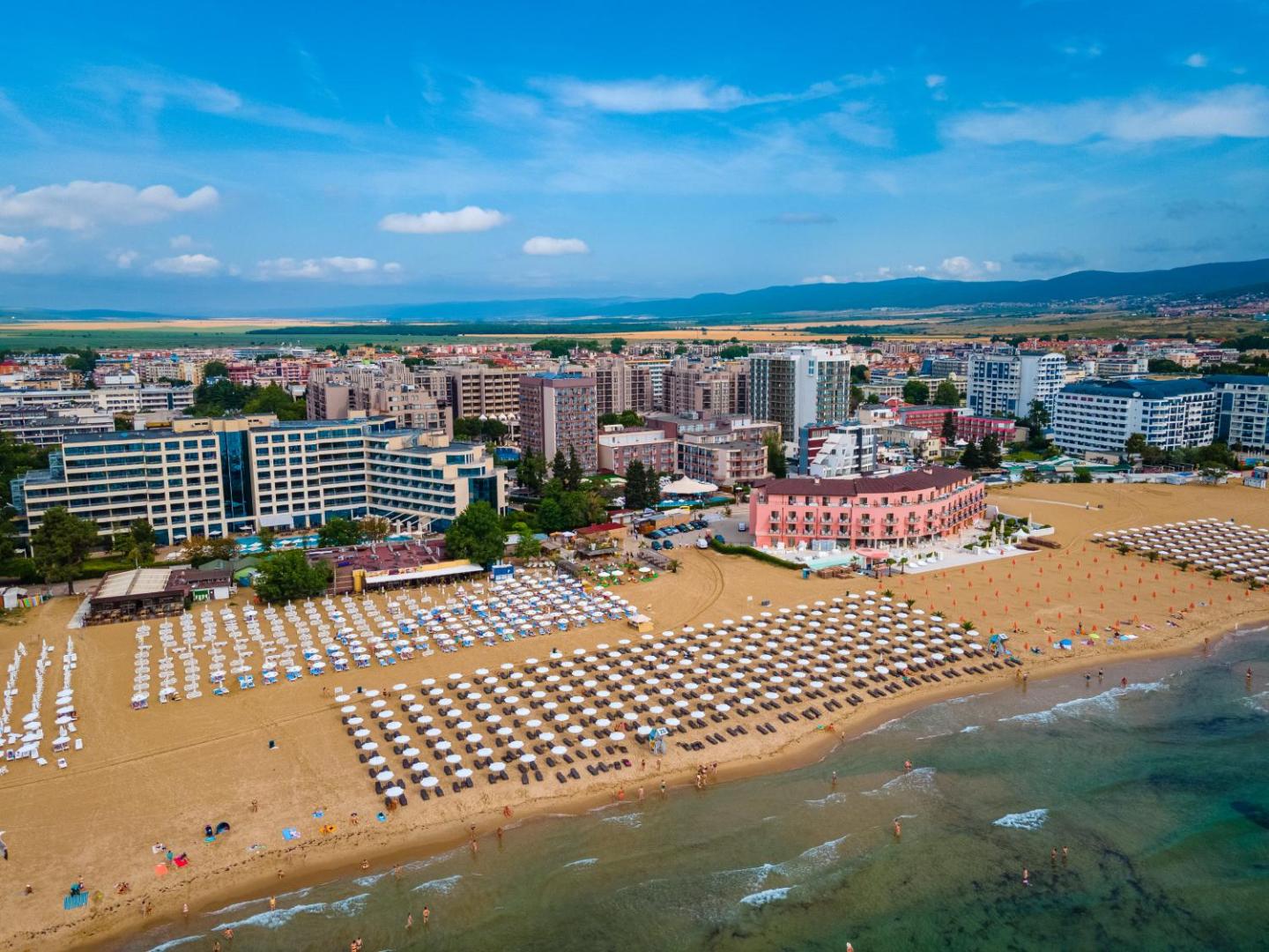 Plašs skats uz Saulainā krasta kūrortu un MPM Hotel Astoria piekrastes zonu ar tūkstošiem saulessargu smilšu pludmalē