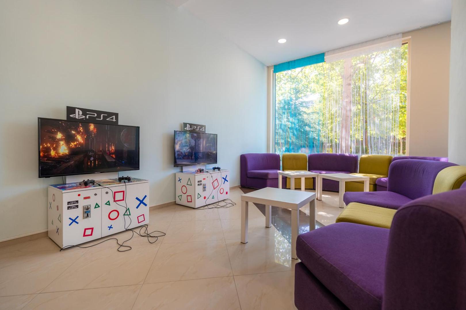 MPM Hotel Astoria spēļu zona ar PlayStation 4 konsolēm un ērtiem dīvāniem — izklaides iespējas bērniem un pusaudžiem viesnīcas telpās