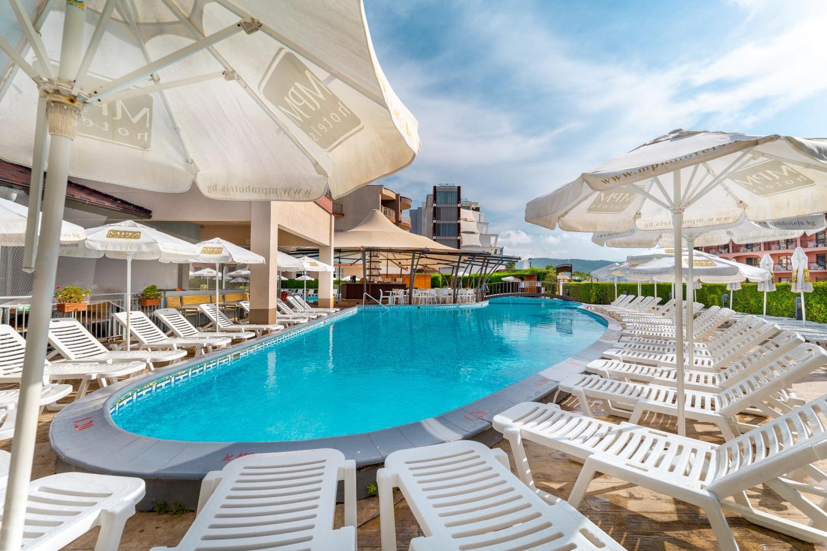 MPM Hotel Astoria āra baseins Saulainajā krastā ar baltiem sauļošanās krēsliem un saulessargiem — atpūtas zona pie ūdens
