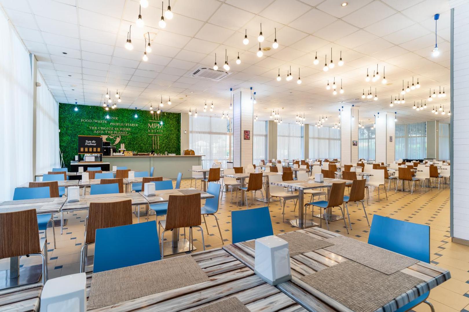 MPM Hotel Astoria galvenais restorāns ar modernu apgaismojumu, gaišām telpām un zilām un brūnām mēbelēm