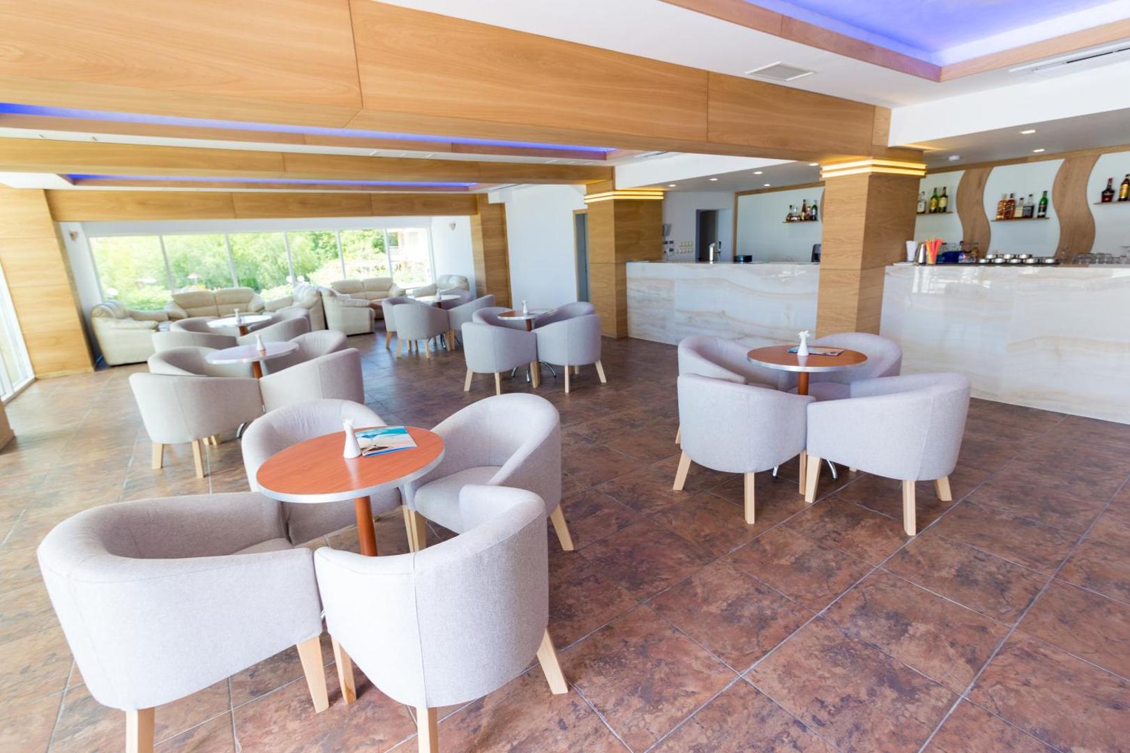 Bilyana Beach Hotel gaišais lobby bārs ar ērtiem atpūtas krēsliem, koka apdari un skatu uz dārzu caur lielajiem logiem