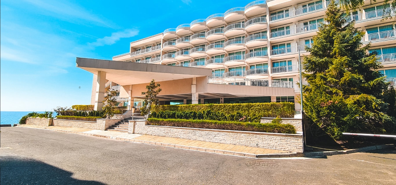 Bilyana Beach Hotel galvenā ieeja un fasāde ar pusapaļiem balkoniem Nesebārā — sakopta teritorija un piebraucamais ceļš
