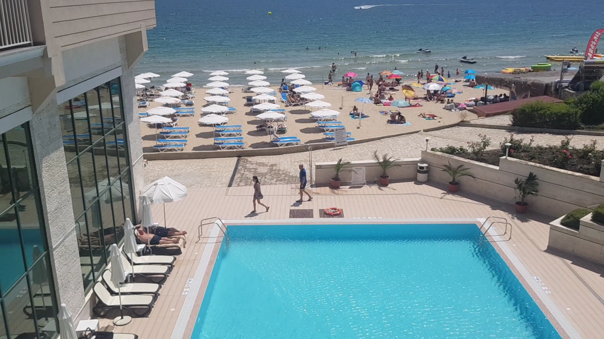 Skats no Bilyana Beach Hotel terases uz āra baseinu un blakus esošo smilšu pludmali ar saulessargiem Melnās jūras krastā