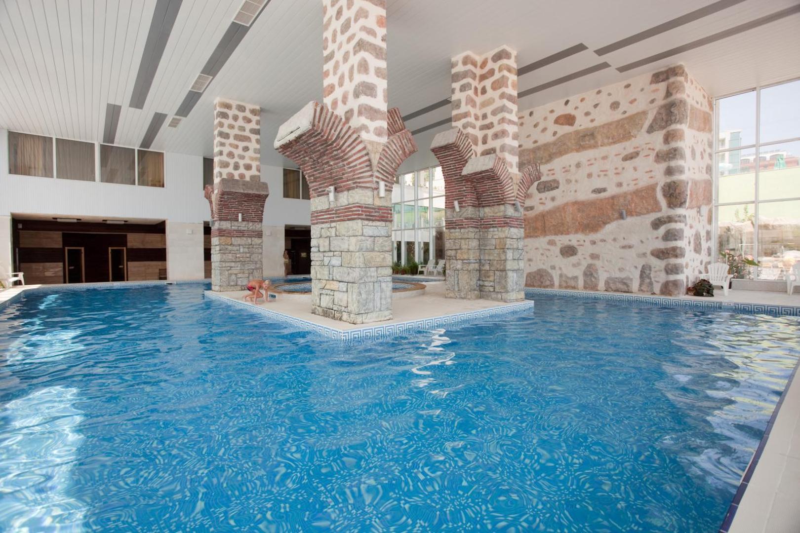 Bilyana Beach Hotel iekštelpu baseins ar masīvām akmens kolonnām un dekoratīvām arkām — plaša spa zona relaksācijai