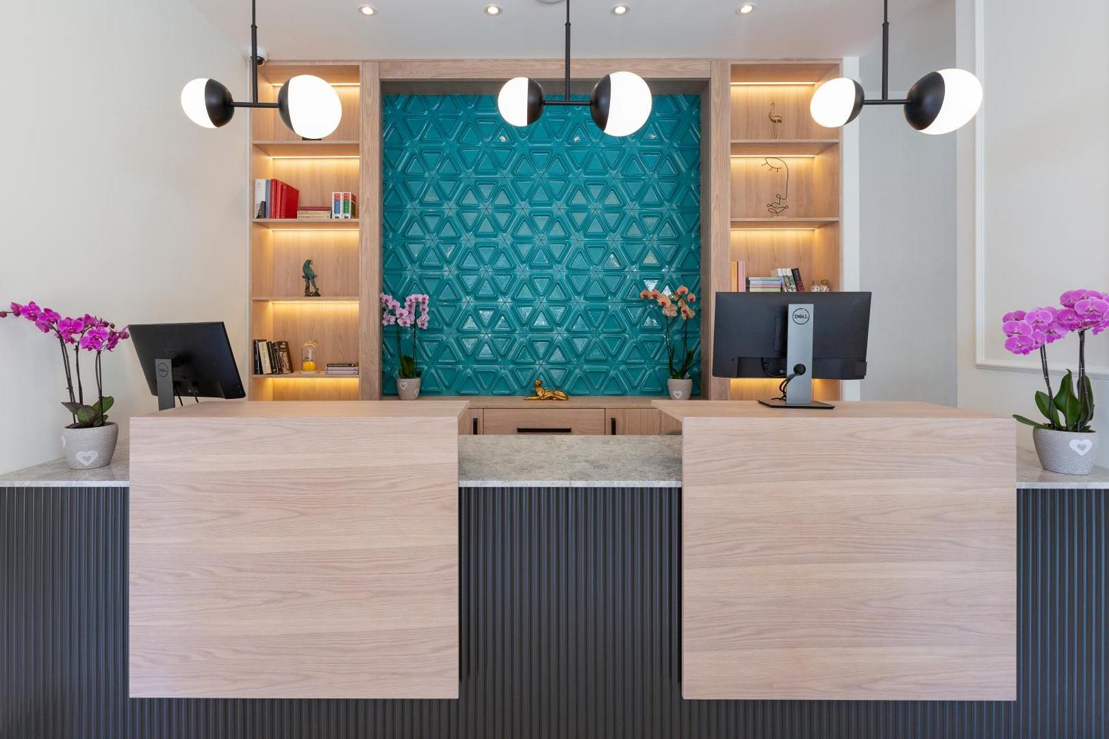 Momentum by Aycon Boutique Hotel recepcijas zona ar modernu koka apdari, tirkīza dekoratīvo sienu un orhidejām Budvā, Melnkalnē