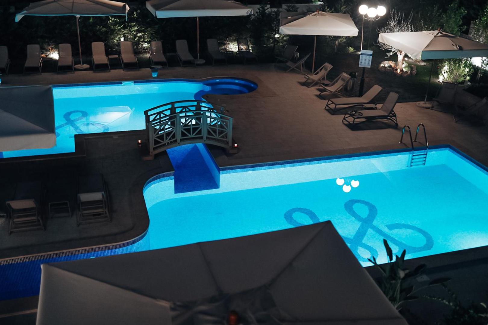 Momentum by Aycon Boutique Hotel baseina zona naktī ar zilu apgaismojumu, dekoratīvu tiltiņu un izgaismotiem lietussargiem Melnkalnē