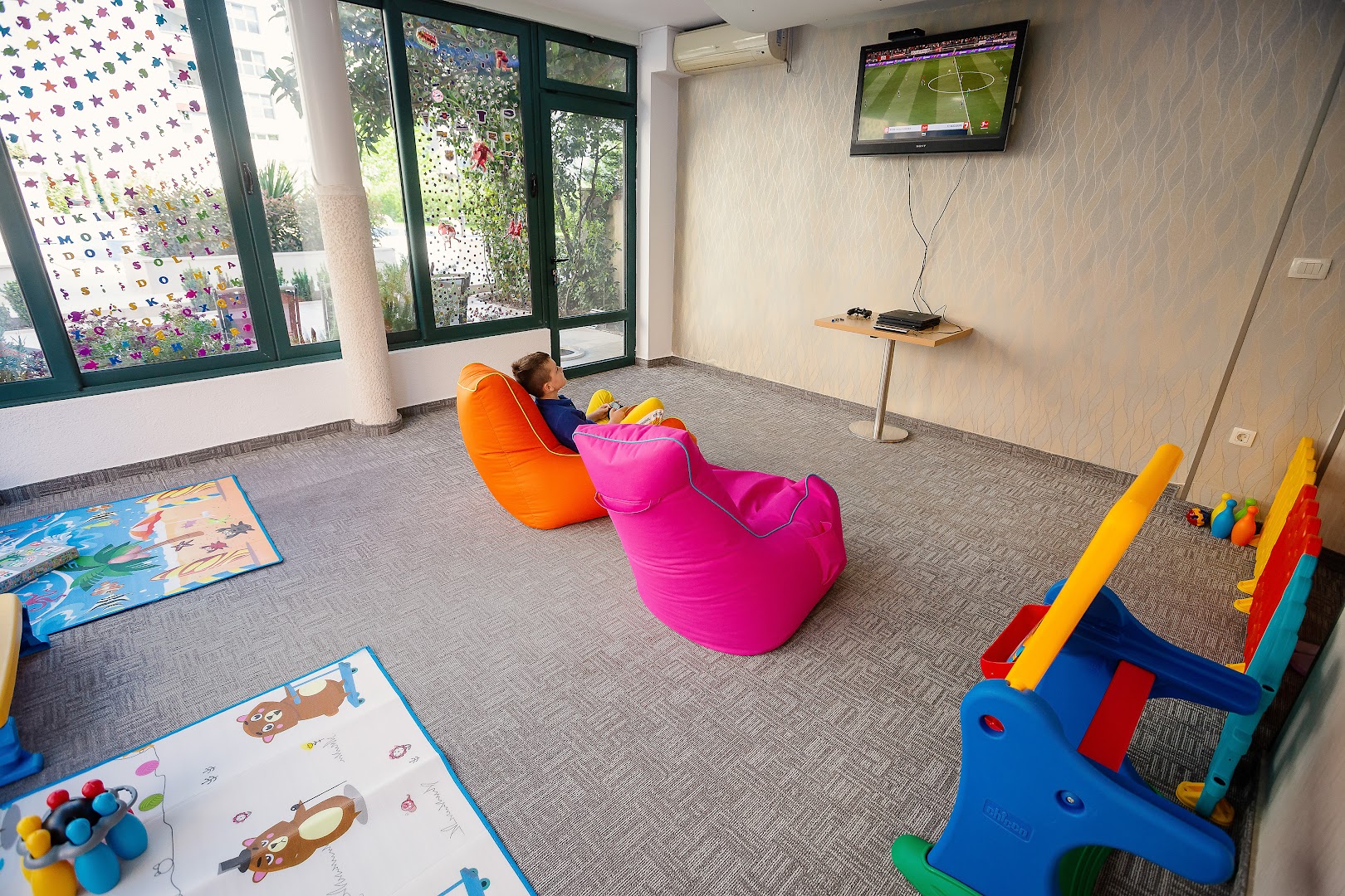 Momentum by Aycon Boutique Hotel bērnu rotaļu istaba ar sēžammaisiem, spēļu konsoli un krāsainiem paklājiem ģimenes atpūtai