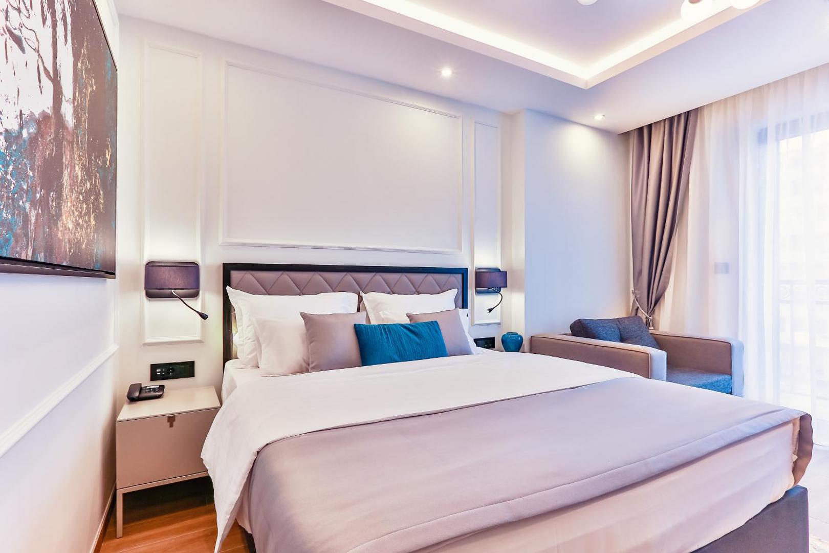 Momentum by Aycon Boutique Hotel gaišs numurs ar divguļamo gultu, dekoratīviem spilveniem un atpūtas krēslu pie loga Budvā, Melnkalnē