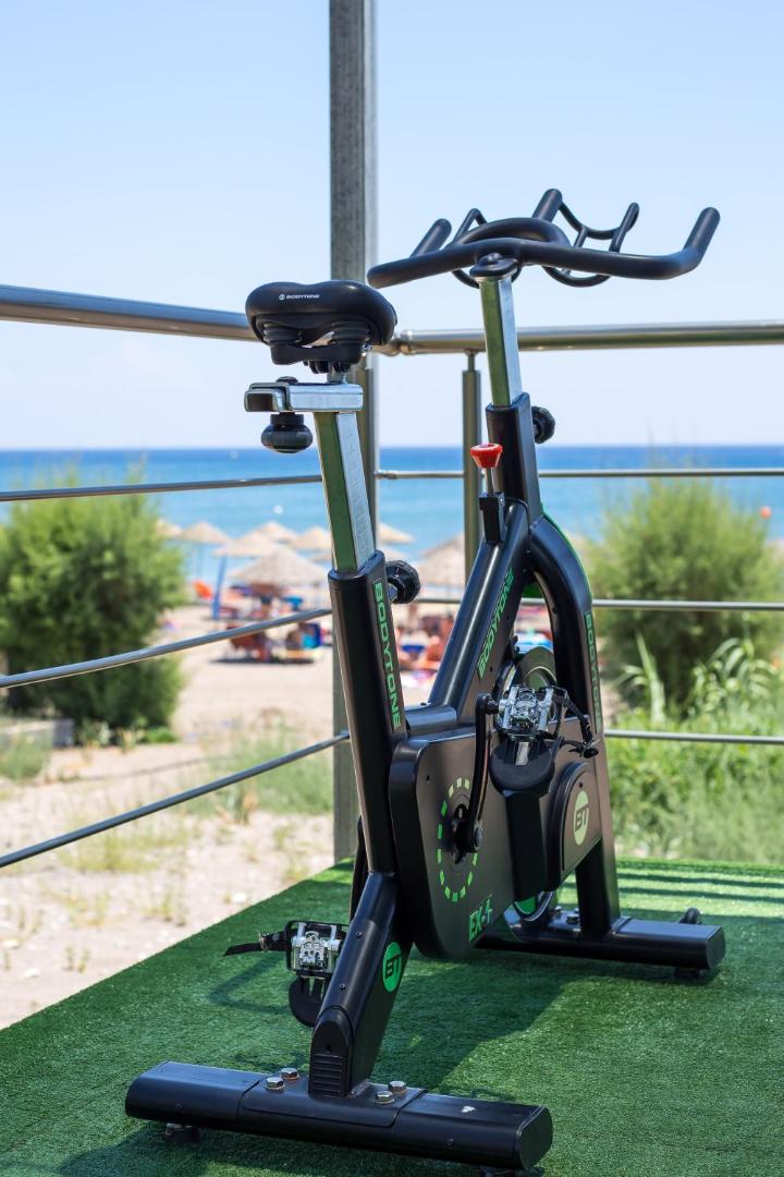 Pegasos Beach Hotel fitnesa velotrenažieris uz āra terases Faliraki, Rodas salā — skats uz pludmali un jūru treniņa laikā