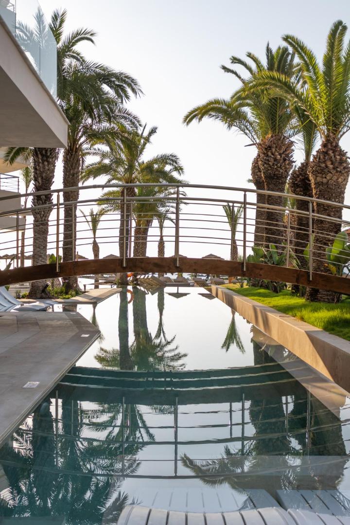 Pegasos Beach Hotel dekoratīvs tilts pār šauru baseinu Rodas kūrortā — palmas un saules atspulgi ūdenī