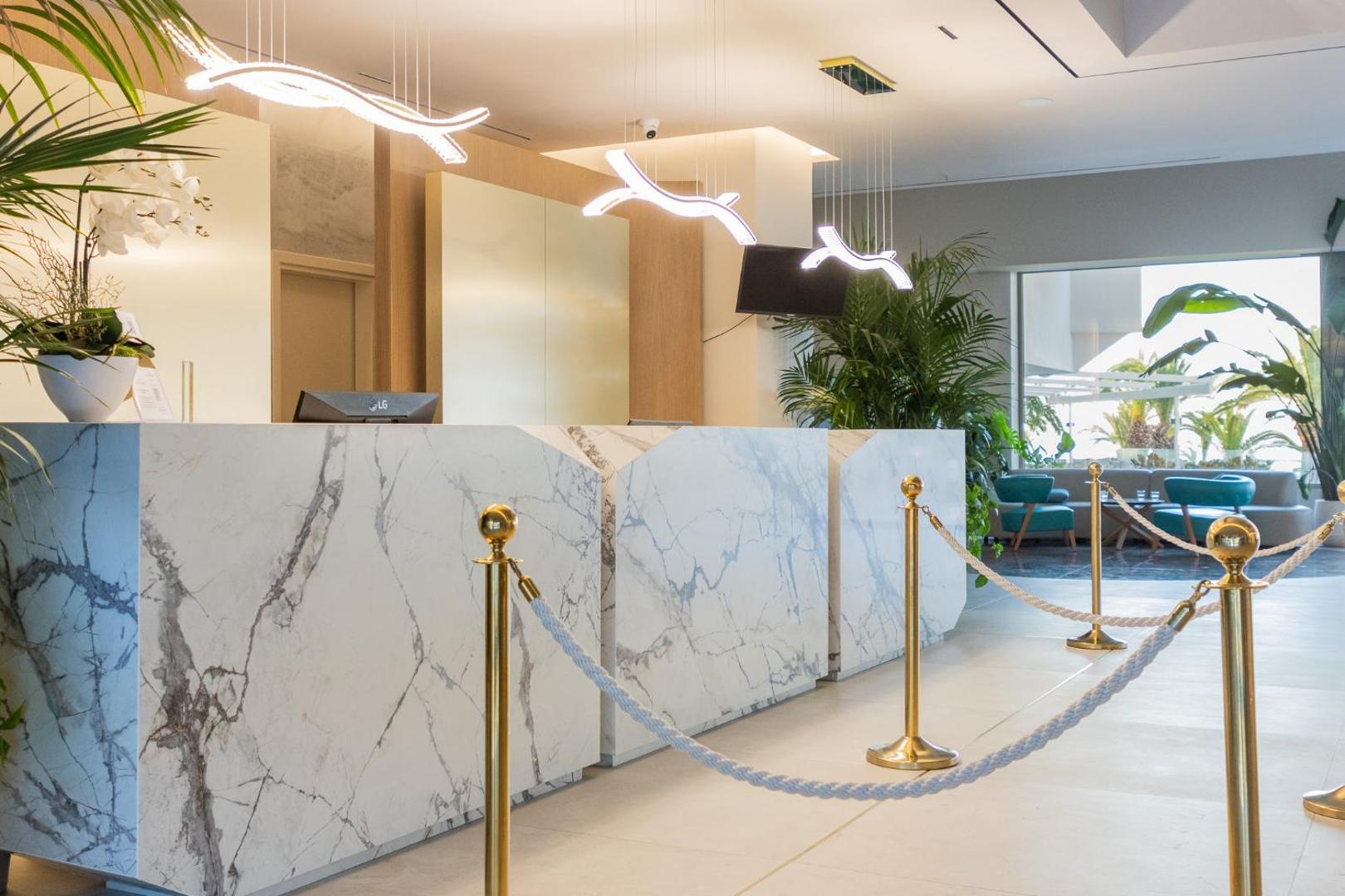 Pegasos Beach Hotel & Resort modernā recepcijas zona ar marmora apdari, dizaina gaismekļiem un zaļajiem augiem Rodā.