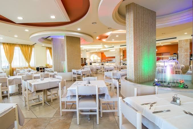 Pegasos Beach Hotel & Resort galvenais restorāns ar gaišu interjeru, dekoratīvām kolonnām un nelielu iekštelpu strūklaku Rodā.