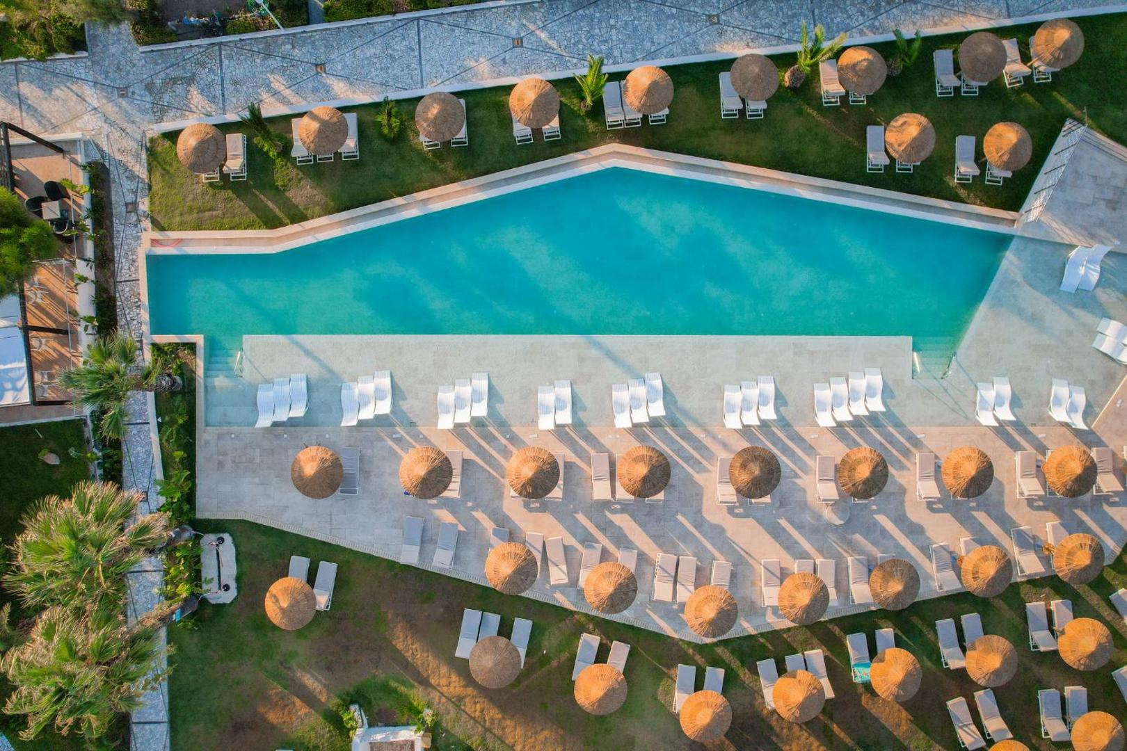 Pegasos Beach Hotel āra baseina skats no augšas ar saulessargiem un zviļņiem zaļā zālājā pie pludmales Rodā