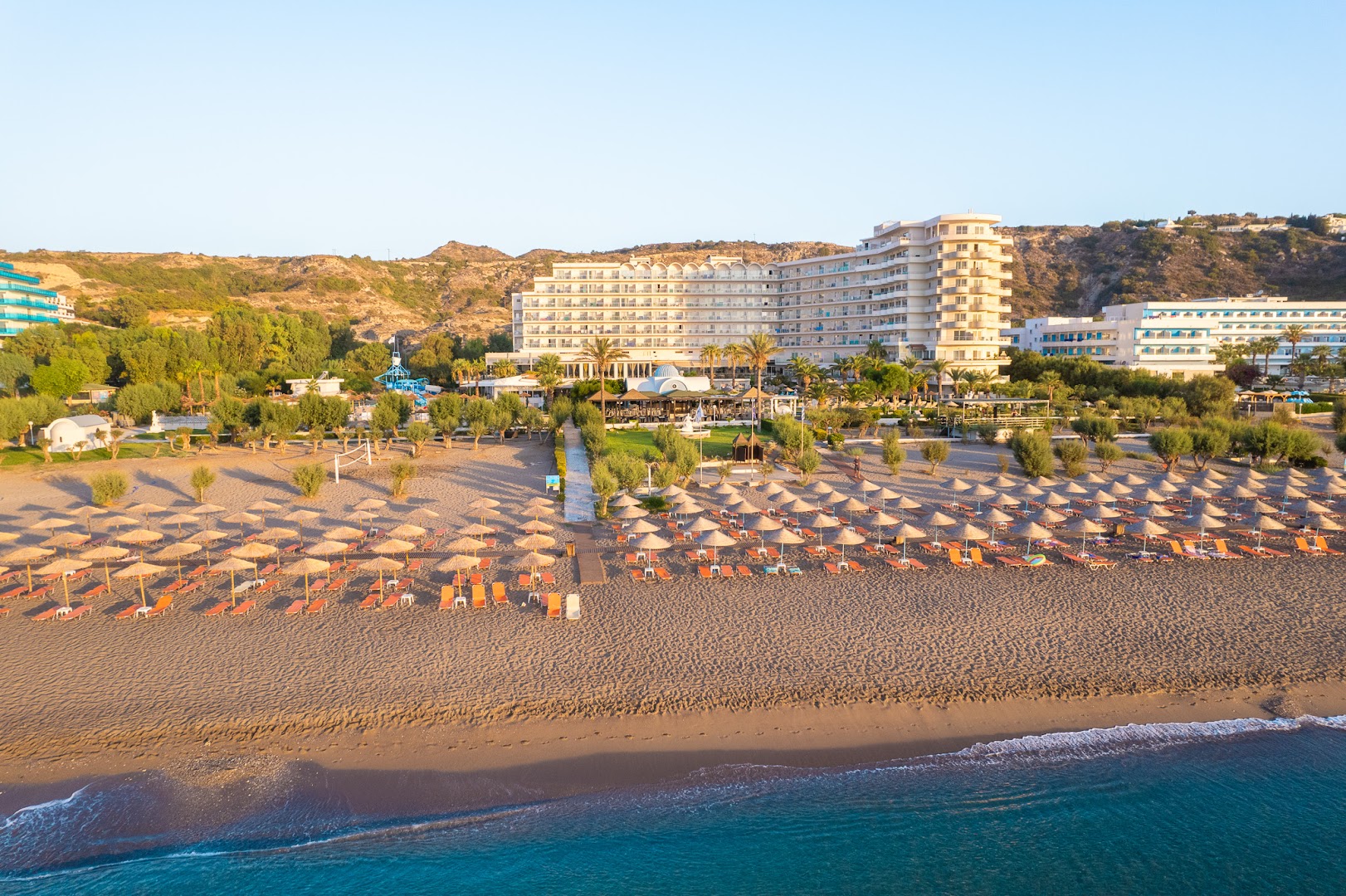 Pegasos Beach Hotel panorāmas skats no putna lidojuma uz plašo smilšu pludmali, saulessargiem un viesnīcas galveno ēku Faliraki piekrastē, Rodas salā.