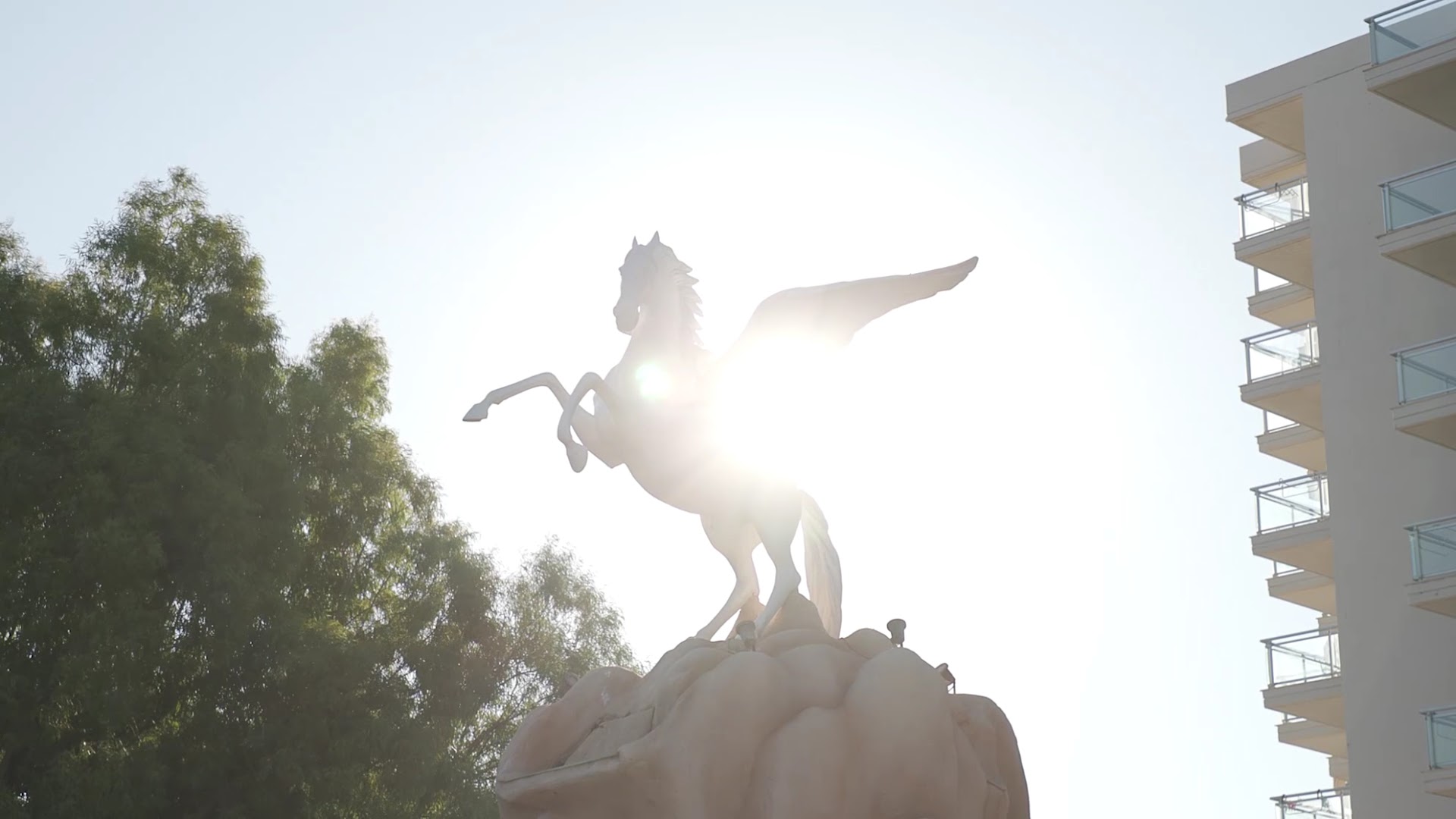 Pegasos Beach Hotel simbols — balta Pegasa statuja saules gaismā pie viesnīcas korpusa Rodas salā, Grieķijā.