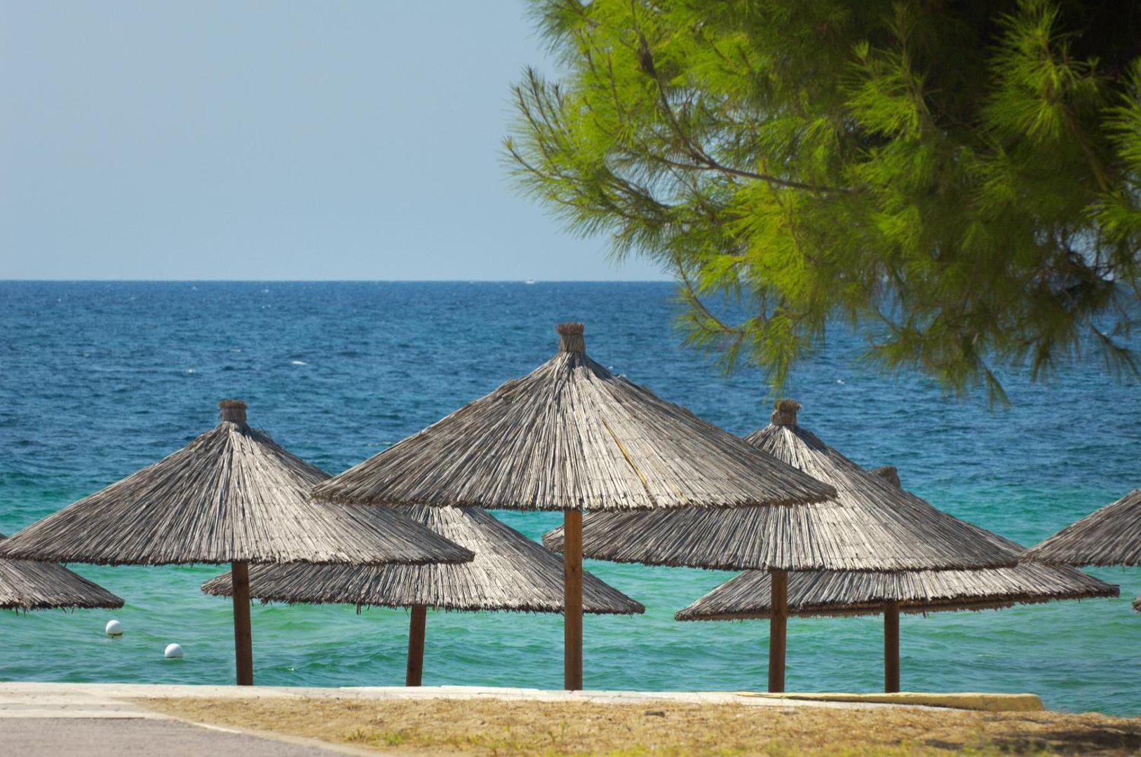 Portes Beach Hotel pludmales zona ar tradicionāliem salmu saulessargiem pie Egejas jūras Halkidiki reģionā, Grieķijā