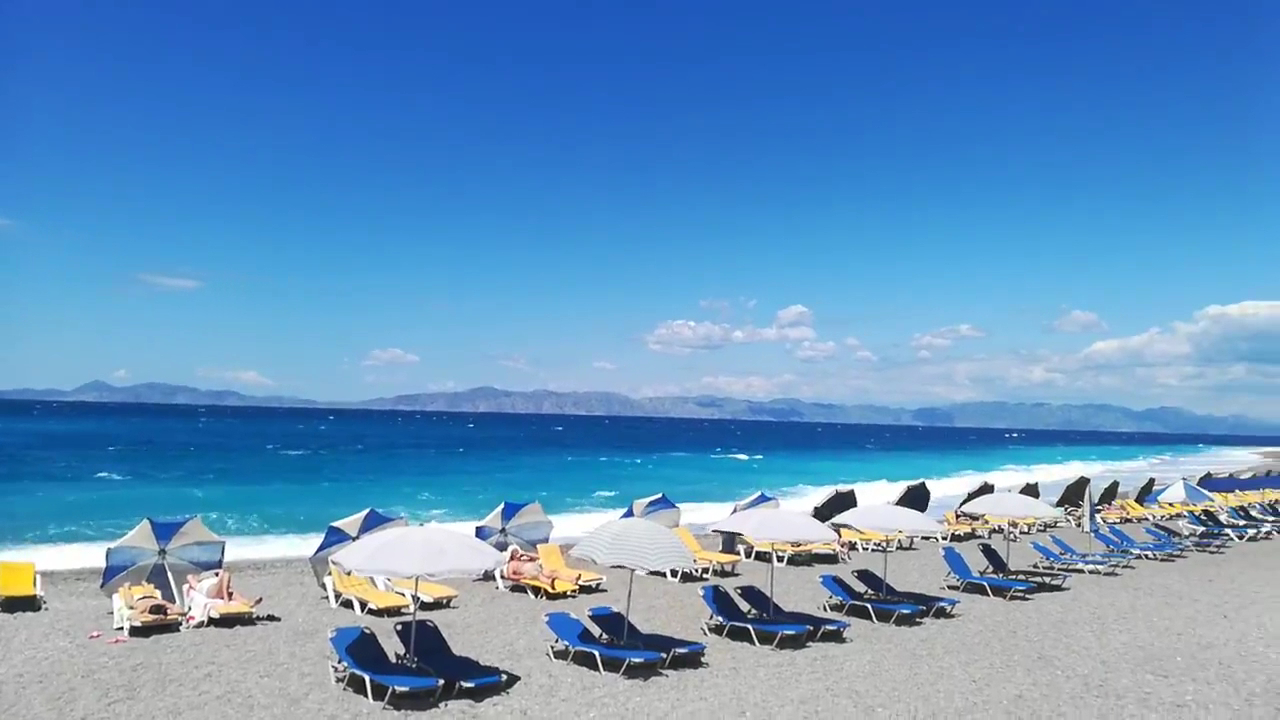 Mitsis La Vita Beach Hotel pludmale ar ziliem sauļošanās krēsliem un saulessargiem pie Egejas jūras Rodā