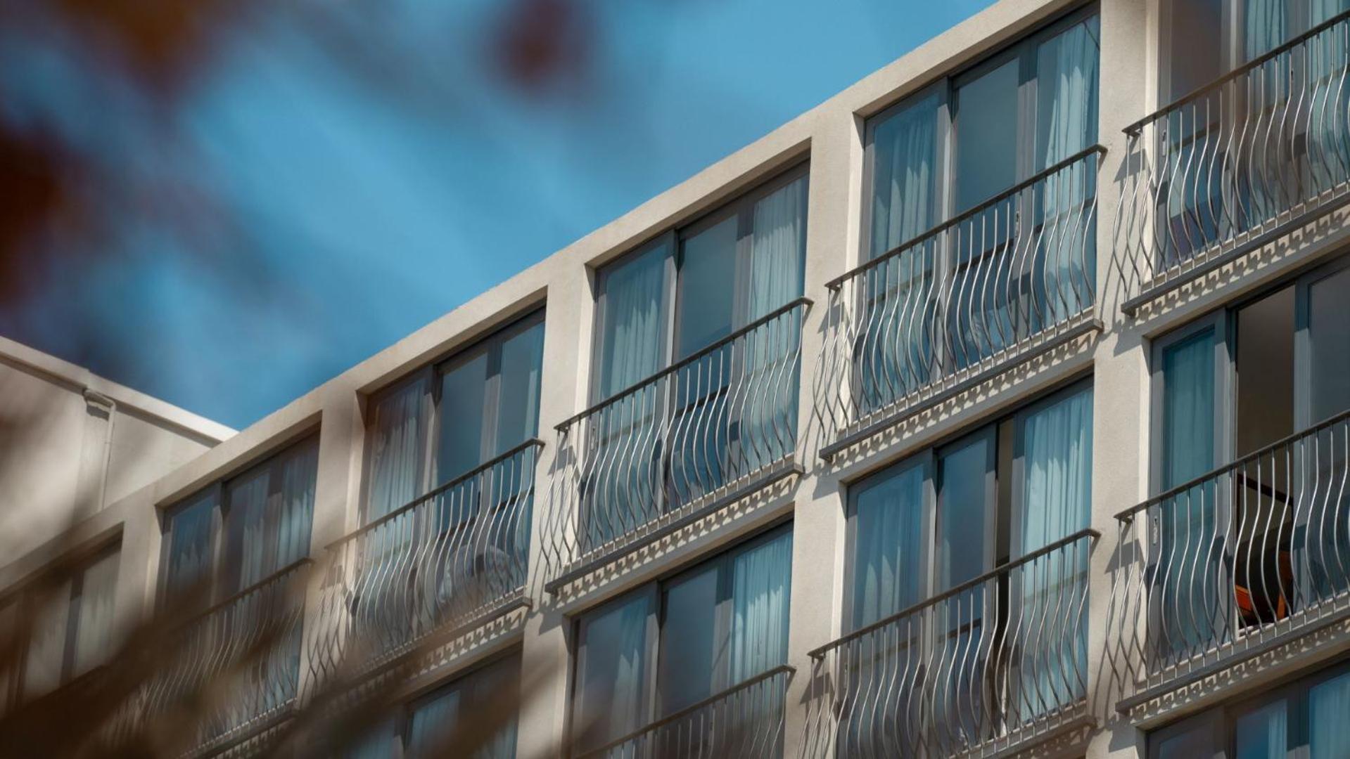 Tuvplāns Mitsis La Vita Beach Hotel numuru balkoniem ar metāla margām un lieliem logiem saulainā dienā