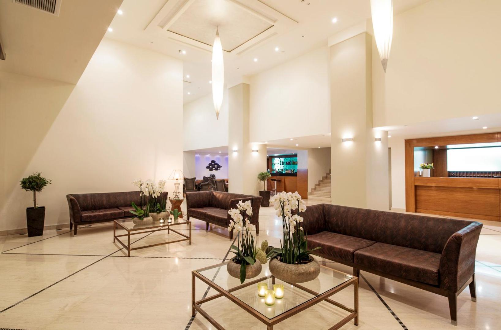 Mitsis La Vita Beach Hotel plašais un gaišais lobby vestibils Rodas pilsētā ar moderniem ādas dīvāniem, stikla galdiņiem un orhideju ziedu dekorācijām.