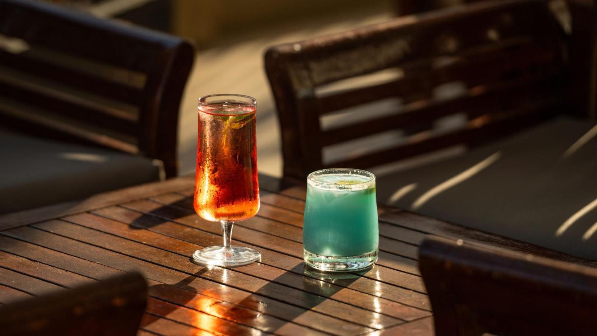 Divi krāsaini atspirdzinoši kokteiļi uz koka galda Mitsis La Vita Beach Hotel terasē saulrieta gaismā Rodas salā.