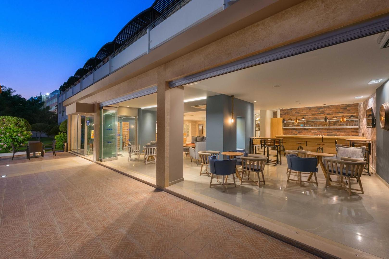 Matoula Beach Hotel atvērtā tipa terase un lobby bārs vakarā ar piekļuvi āra zonai un ērtiem atpūtas krēsliem