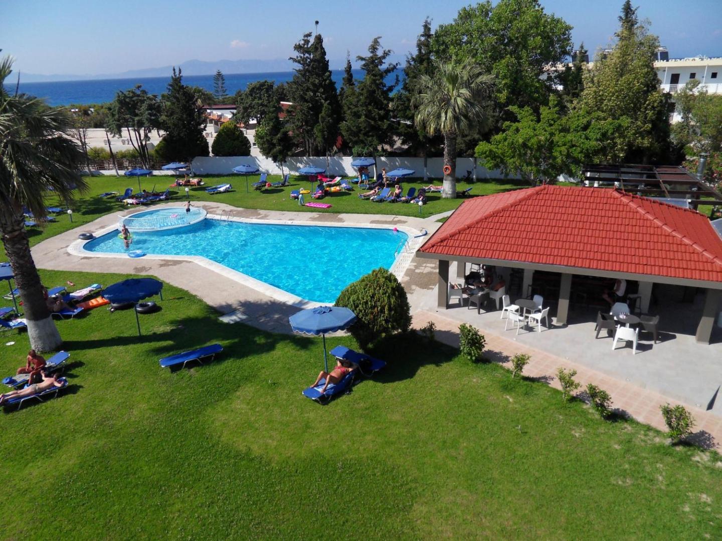 Matoula Beach Hotel teritorijas skats no augšas — baseins, bērnu zona un bārs zaļā dārzā ar skatu uz jūru tālumā