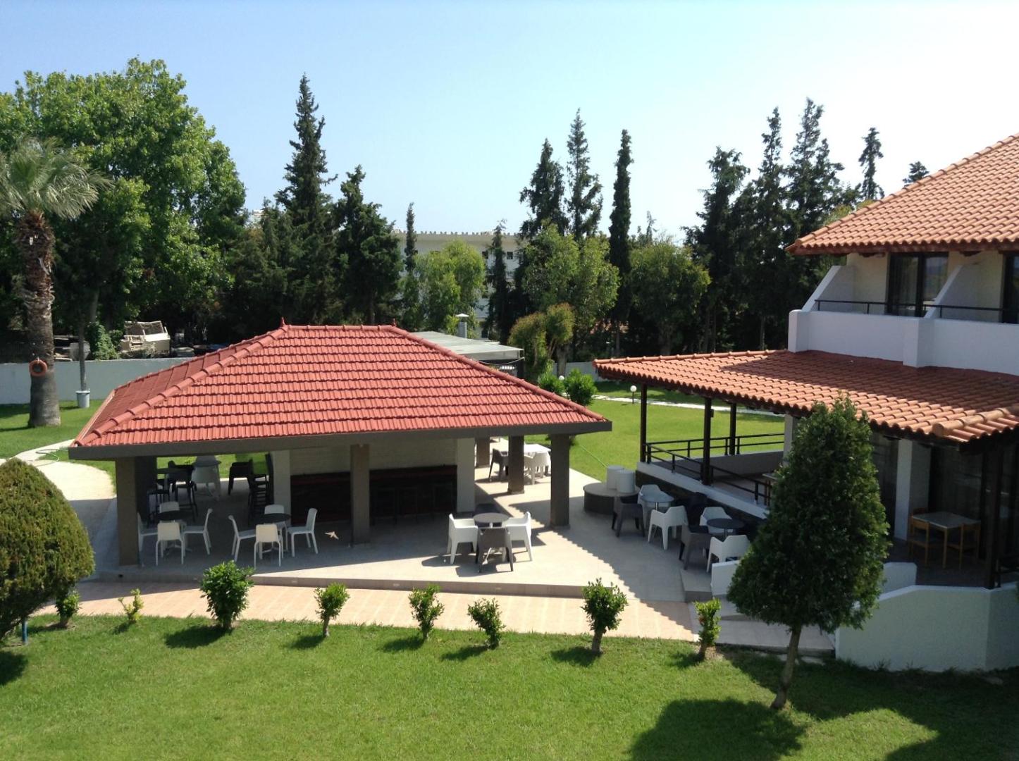 Matoula Beach Hotel āra uzkodu bārs ar dakstiņu jumtu un galdiņiem Rodas salā, apkārt zaļojošs dārzs un koki