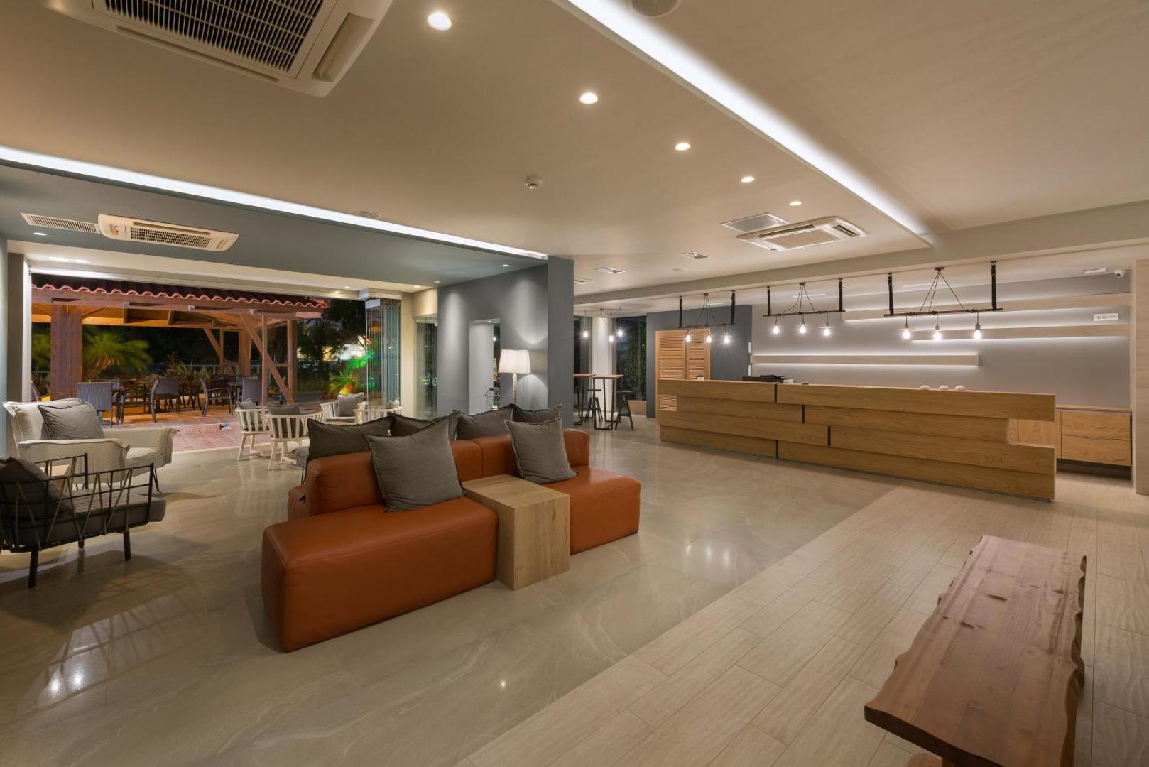 Matoula Beach Hotel plašais lobby un atpūtas zona ar moderniem dīvāniem, koka recepcijas leti un siltu apgaismojumu vakarā
