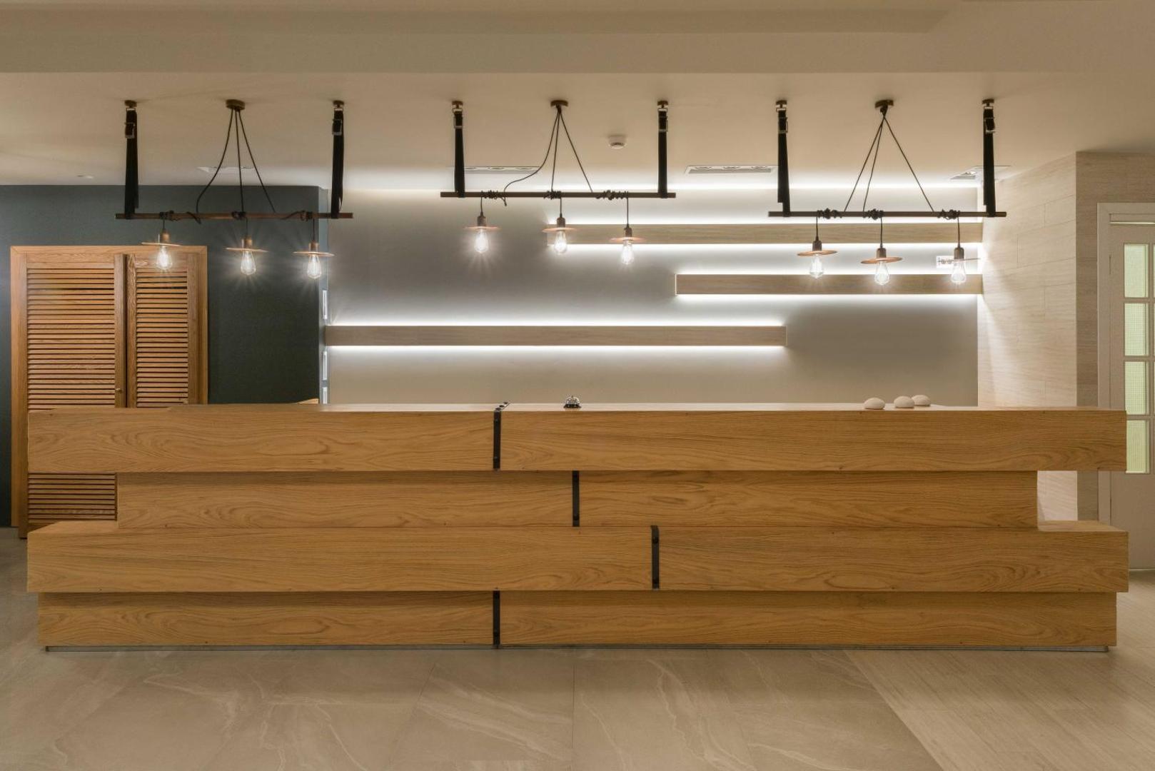 Matoula Beach Hotel recepcijas lete no dabīga koka ar dizaina lampām un minimālistisku interjeru viesnīcas galvenajā ēkā