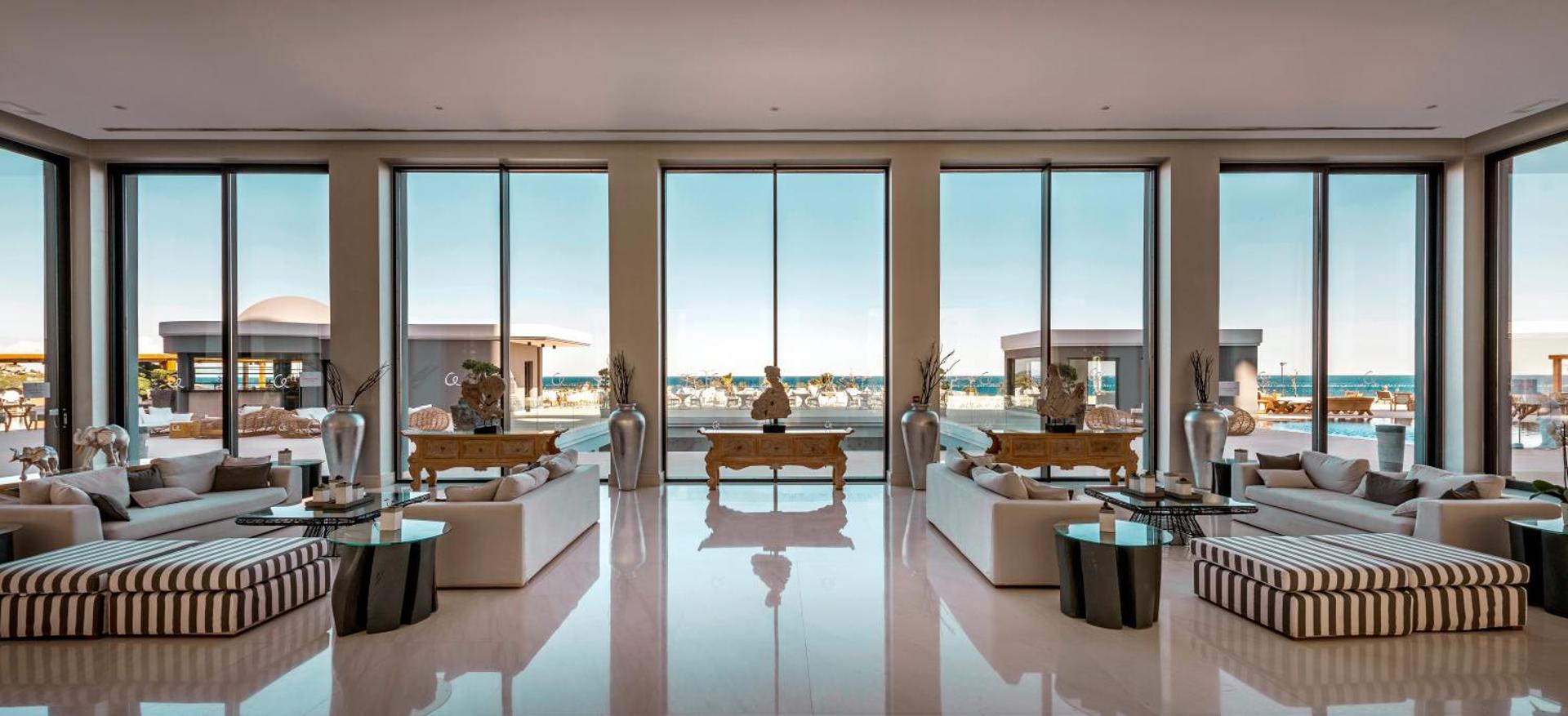 Mitsis Selection Alila viesnīcas plašā lobby atpūtas zona ar skatu uz jūru Rodas salā, Grieķijā — eleganti dīvāni un panorāmas logi