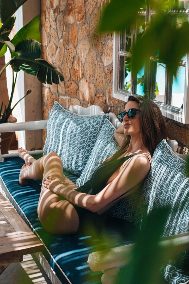 Atpūtas zona ar mīkstiem spilveniem Danaides Apartments terasē Malijā — akmens sienas un tropu augu ēnas