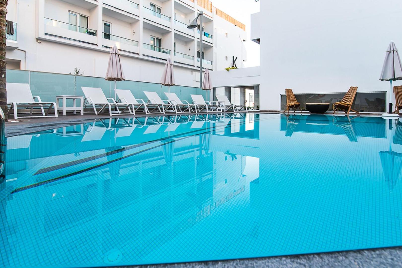 Tuvplāns Kahlua Boutique Hotel baseinam ar dzidru ūdeni un atspulgiem — fonā rindā izvietoti balti sauļošanās krēsli un saulessargi